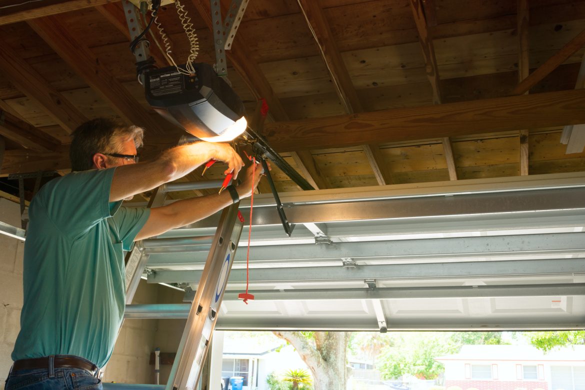 Professional automatic garage door opener repair service technician man working Professional automatic garage door opener repair service technician man working on a ladder at a home residential location making adjustments and fixing it while installing it.